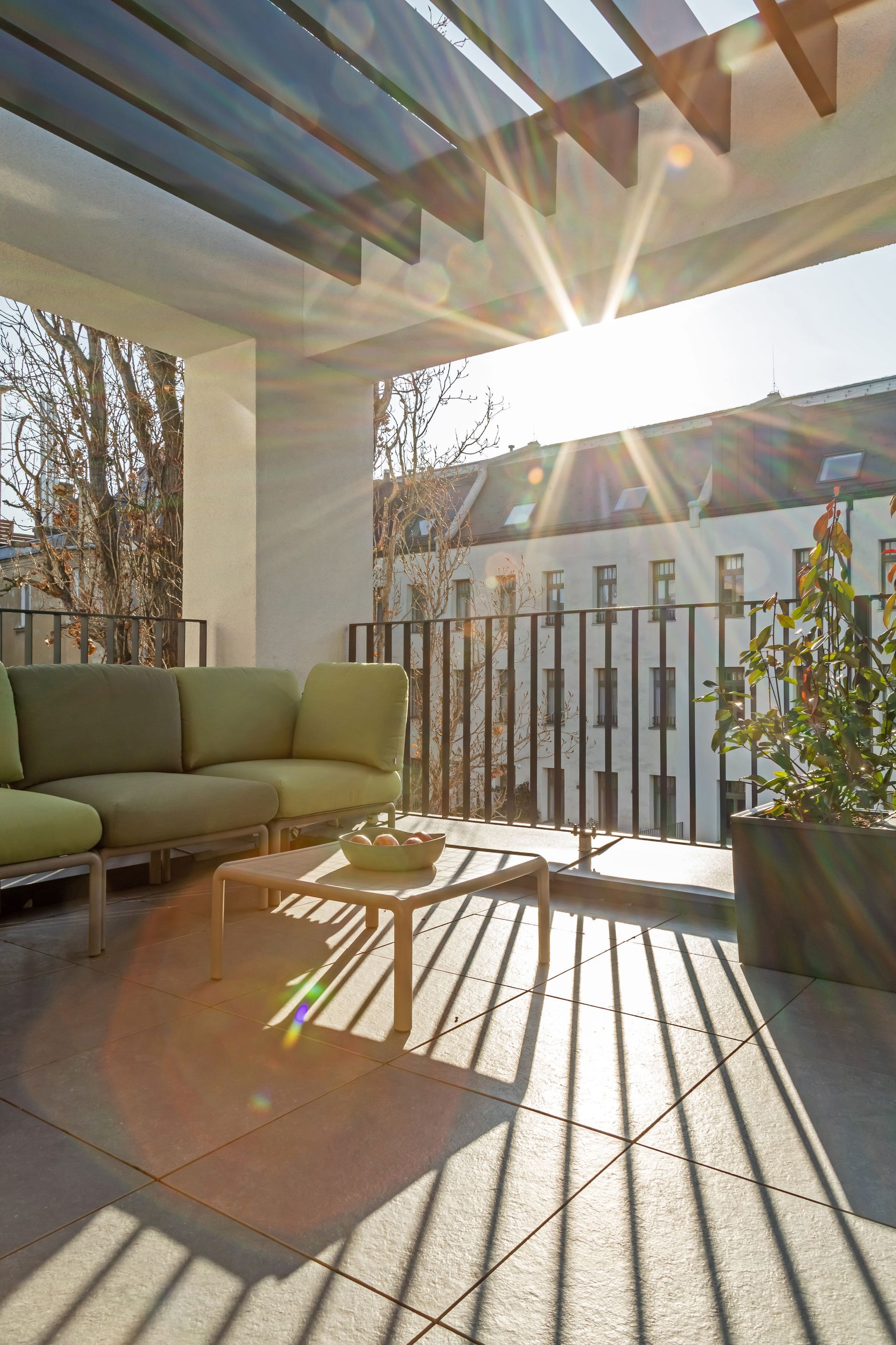 Outdoor patio with green couch, coffee table, and overhead pergola, bathed in sunlight in Marone Suites Budapest.