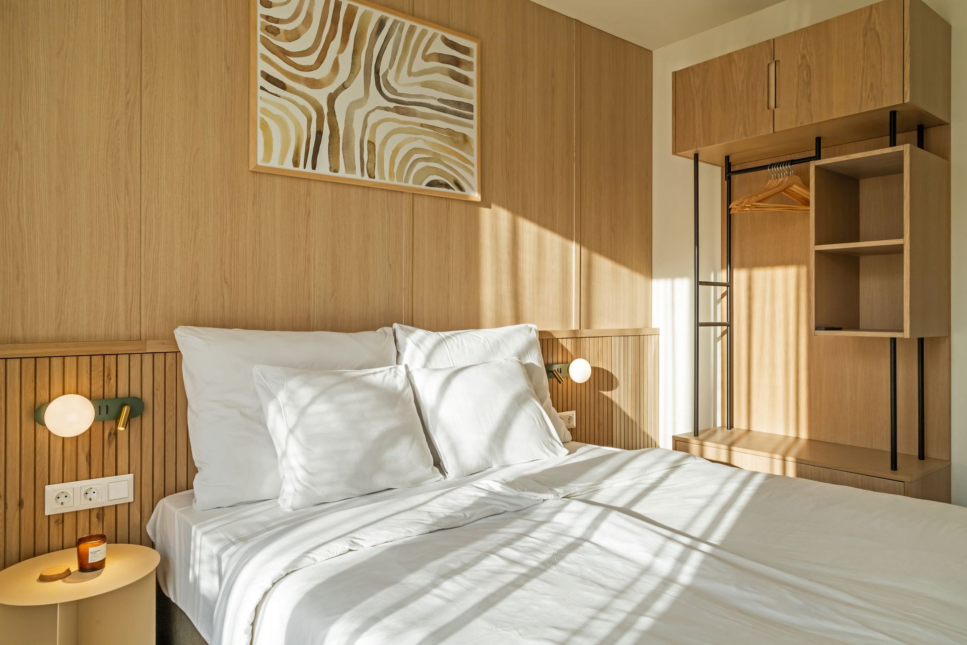 Bedroom with a bed, wooden paneling, art, an open closet, and sunlight in Marone Suites Budapest.