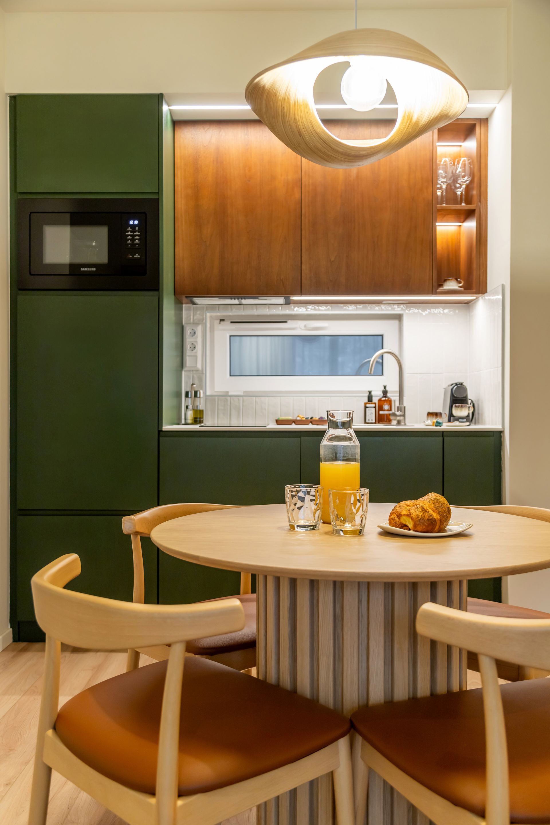 Modern kitchen with olive green cabinets, wooden accents, and a round wooden table with chairs in Marone Suites Budapest.