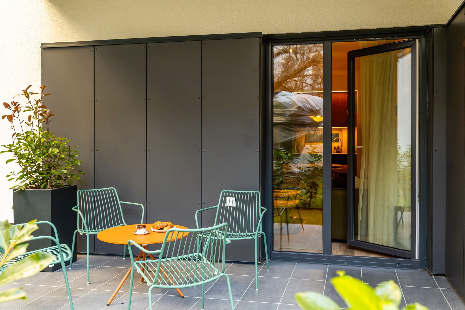 Garden patio with metal furniture, next to dark wall and open glass door in Marone Suites Budapest.