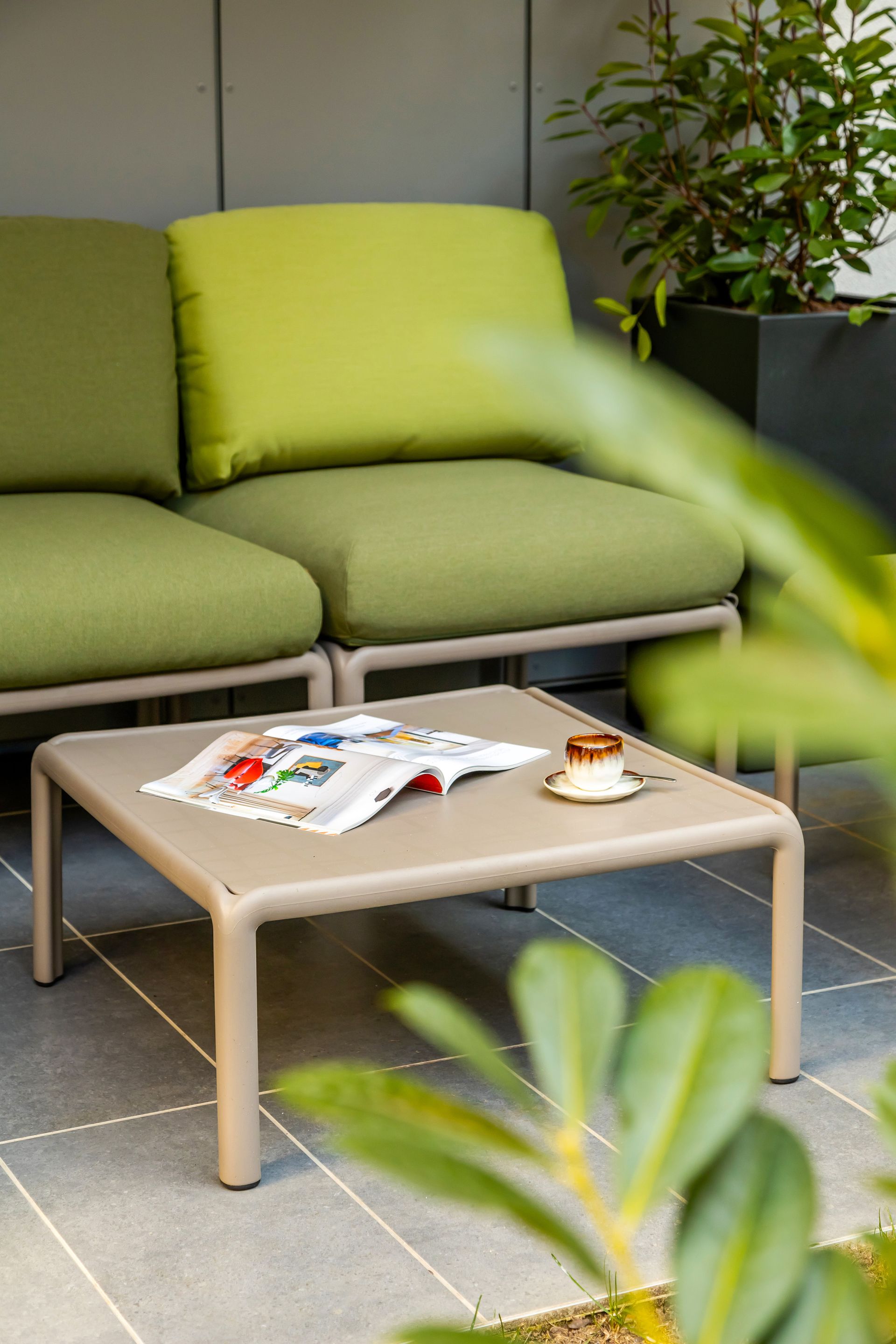 Outdoor seating area with olive green cushions, beige coffee table, and a potted plant in Marone Suites Budapest.