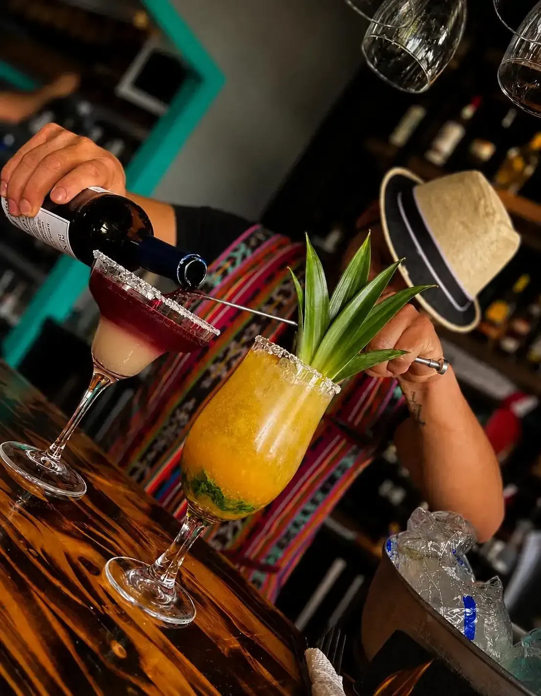 Un camarero sirve vino tinto en un cóctel amarillo adornado con piña en un bar.