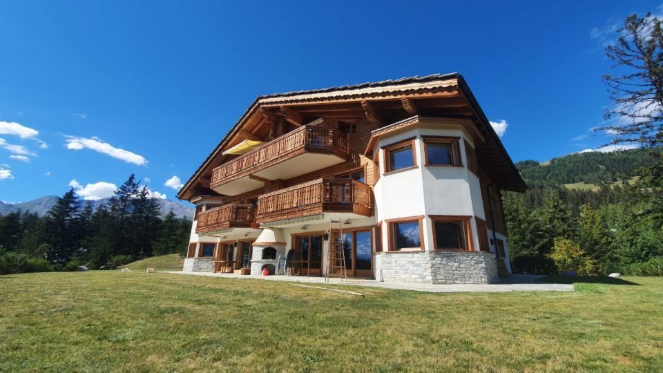 Une grande maison est située au sommet d'une colline verdoyante entourée d'arbres.