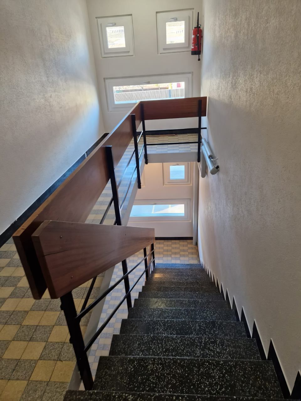 Un escalier avec une rampe en bois et un extincteur sur le mur