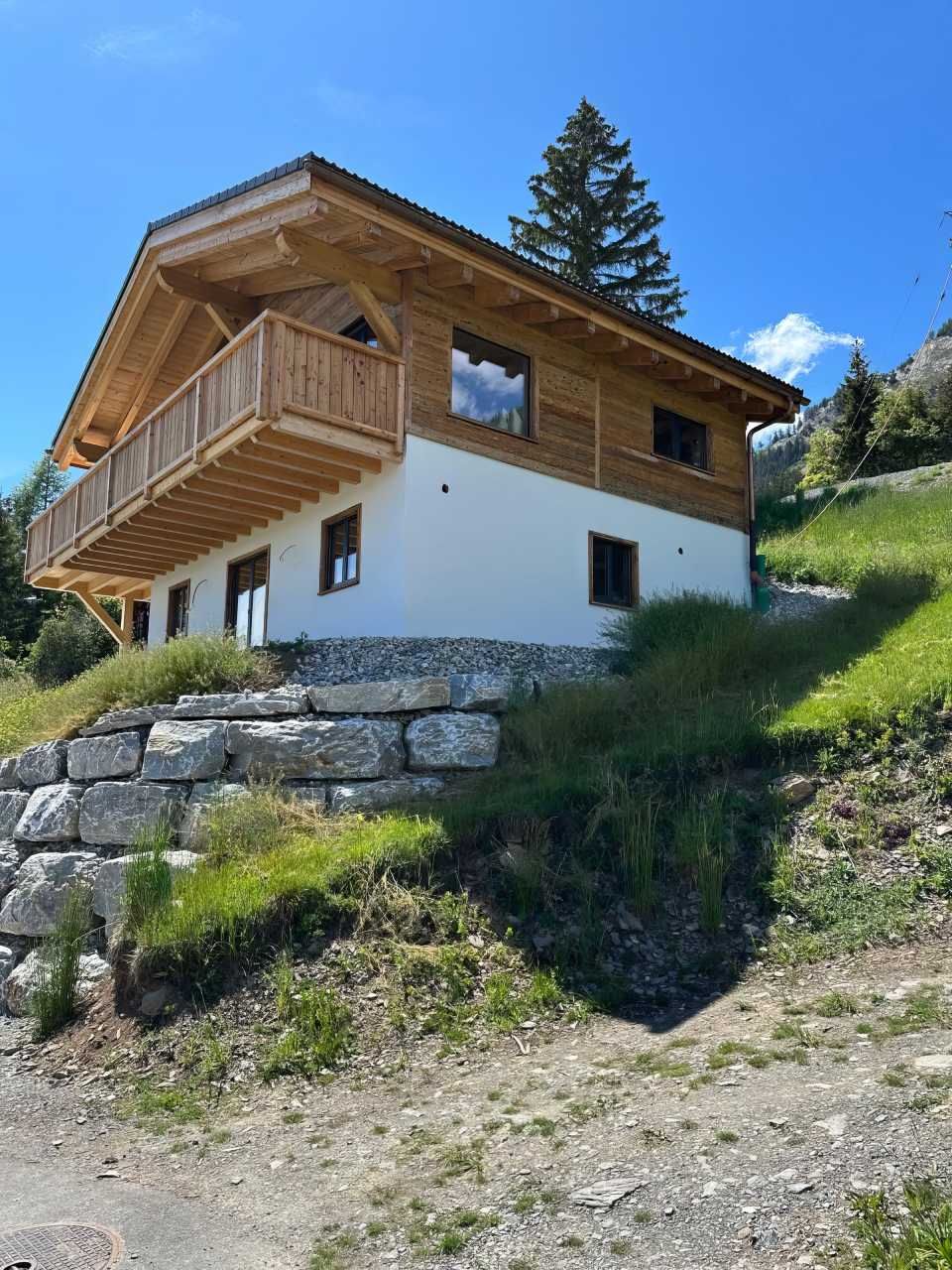Une maison blanche avec une terrasse en bois est située au sommet d'une colline.