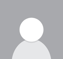 Un homme portant un pull gris et des lunettes de soleil se tient devant un mur rayé noir et blanc.