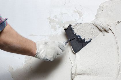 Un homme enduit un mur avec une spatule.