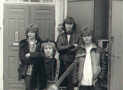 Ryhmä nuoria miehiä seisoo oven edessä kitaroita kädessään.