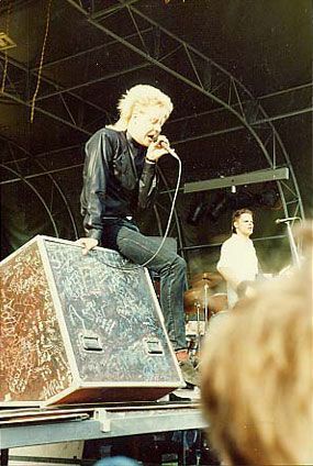 Mies istuu kaiuttimen päällä ja laulaa mikrofoniin.