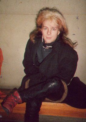 Mustassa takissa ja punaisissa saappaissa oleva nainen istuu penkillä