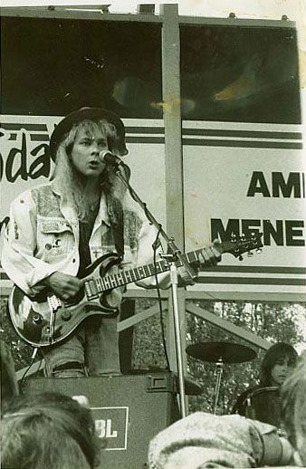 Mustavalkoinen valokuva miehestä soittamassa kitaraa ja laulamassa mikrofoniin.