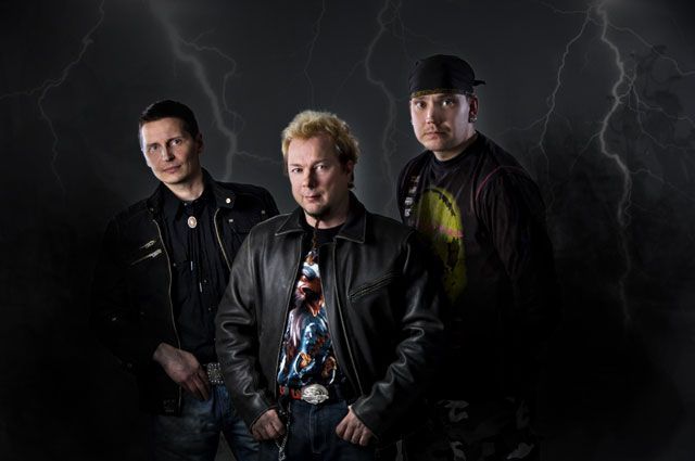 Kolme miestä seisoo vierekkäin pimeässä huoneessa, jonka taustalla loisti salama.