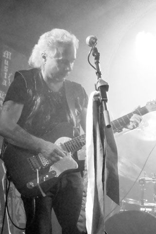 Mies soittaa kitaraa mikrofonin edessä mustavalkoisessa valokuvassa.