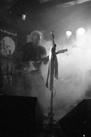 Mies soittaa kitaraa lavalla mustavalkoisessa valokuvassa.