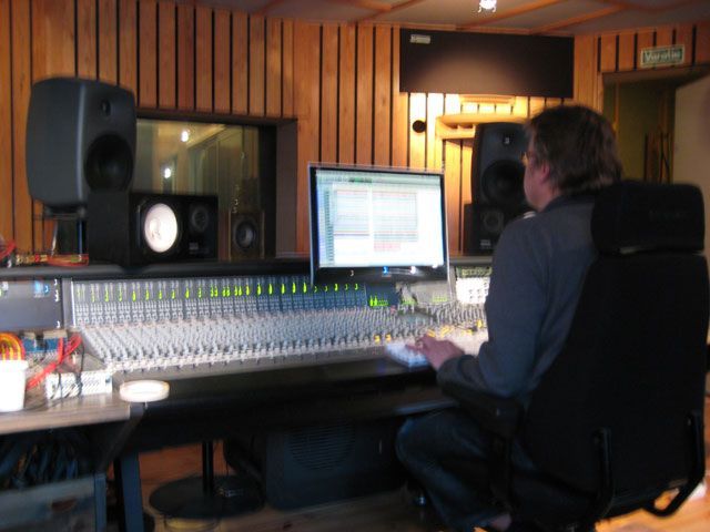 Mies istuu tietokoneen ääressä äänitysstudiossa