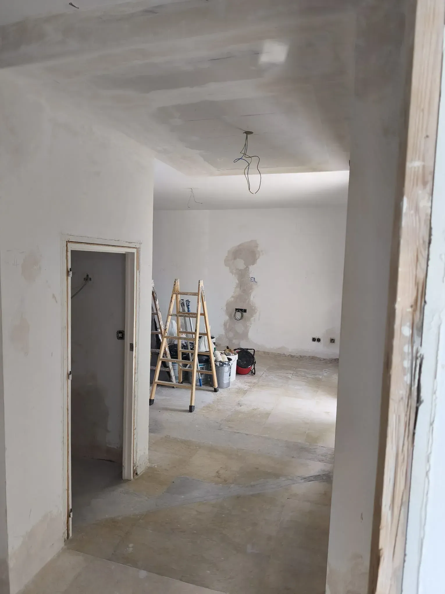 Vista interior de una habitación en remodelación, con paredes expuestas, escalera y cables colgando del techo.
