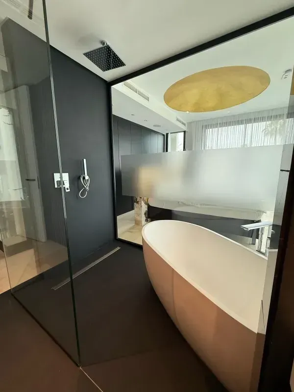 Baño moderno con bañera independiente, ducha de cristal, paredes oscuras y espejo grande.