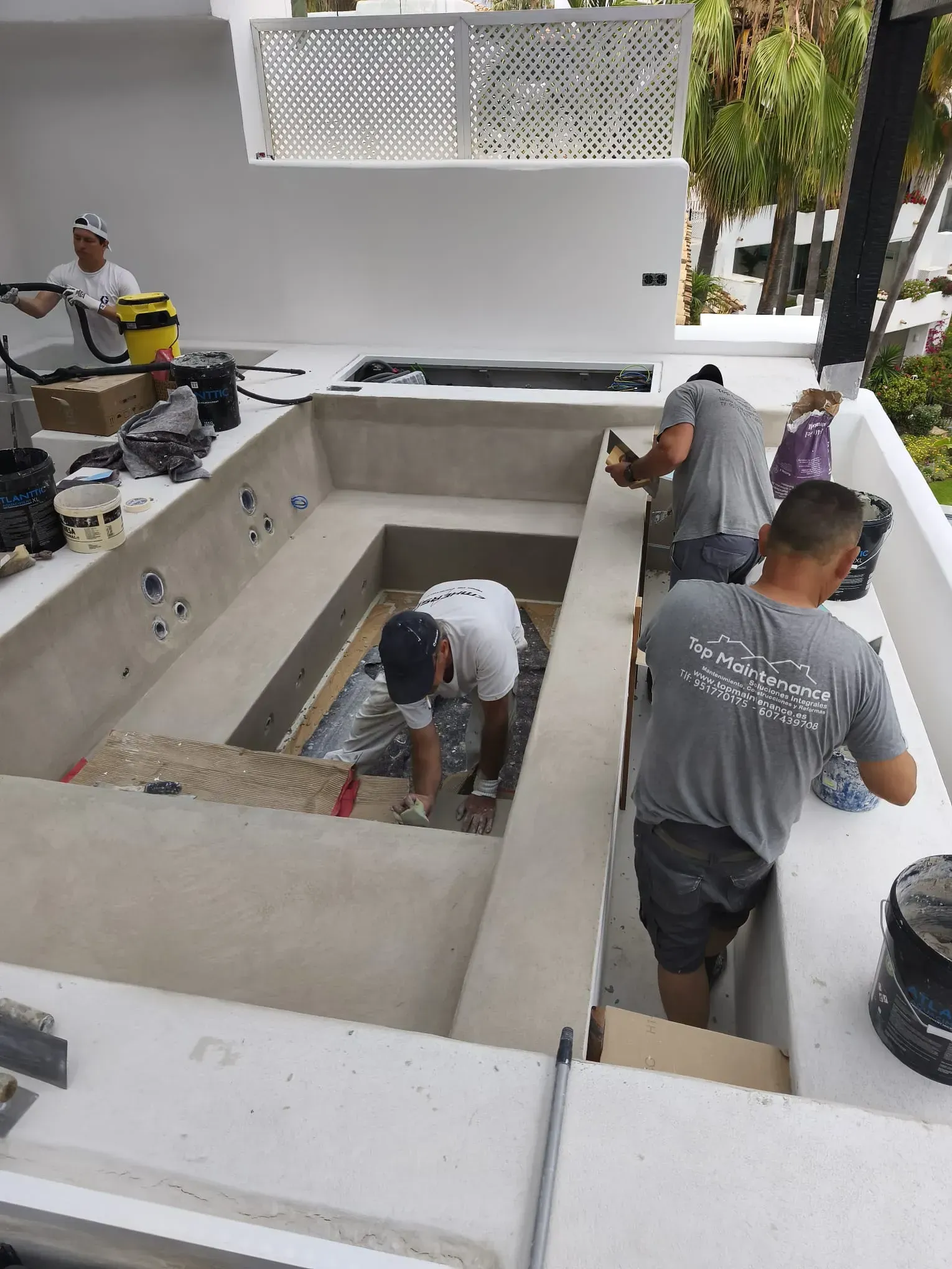 Trabajadores alicatando una piscina sobre un tejado blanco. Están aplicando lechada. Hay otros equipos cerca.