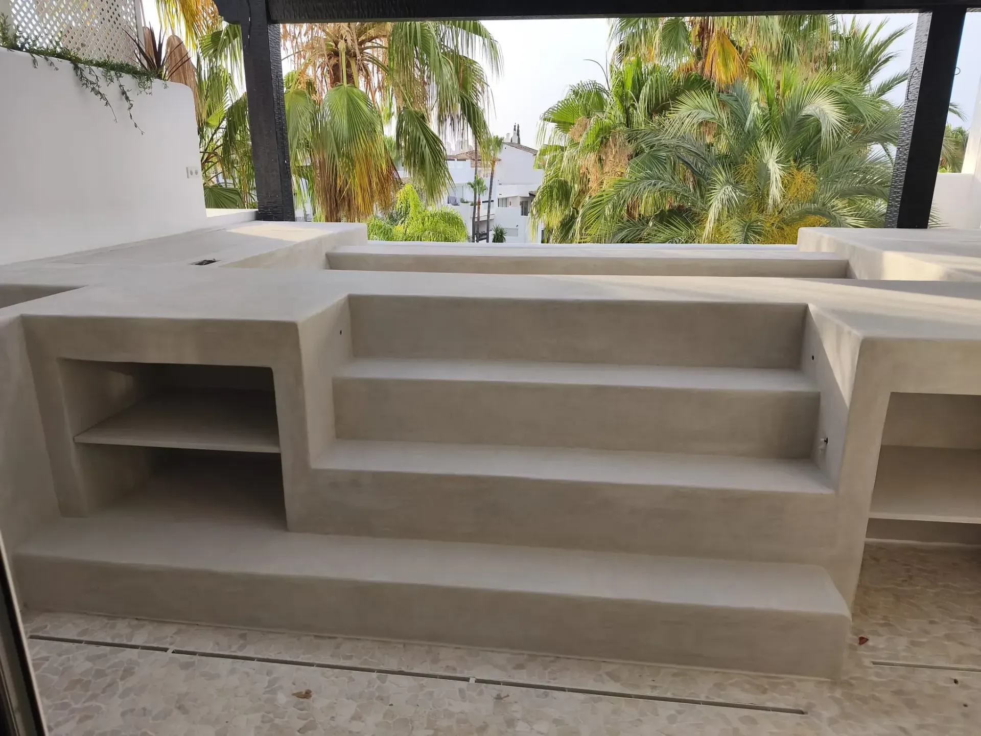 Escaleras y estanterías exteriores de hormigón, con frondosas palmeras al fondo.