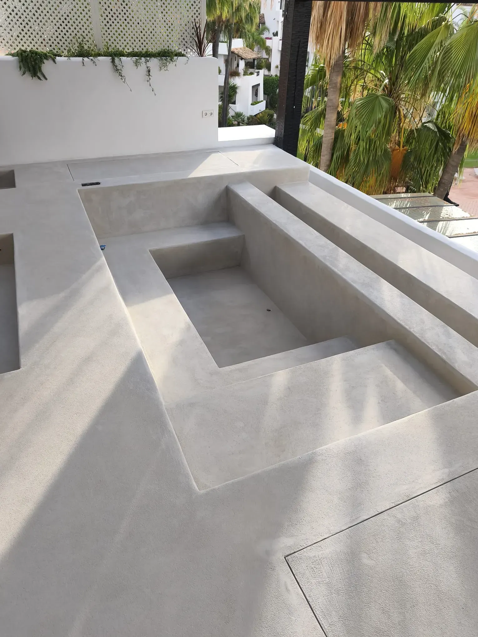 Patio de hormigón con escalones empotrados y un estanque rectangular. Luz solar intensa.