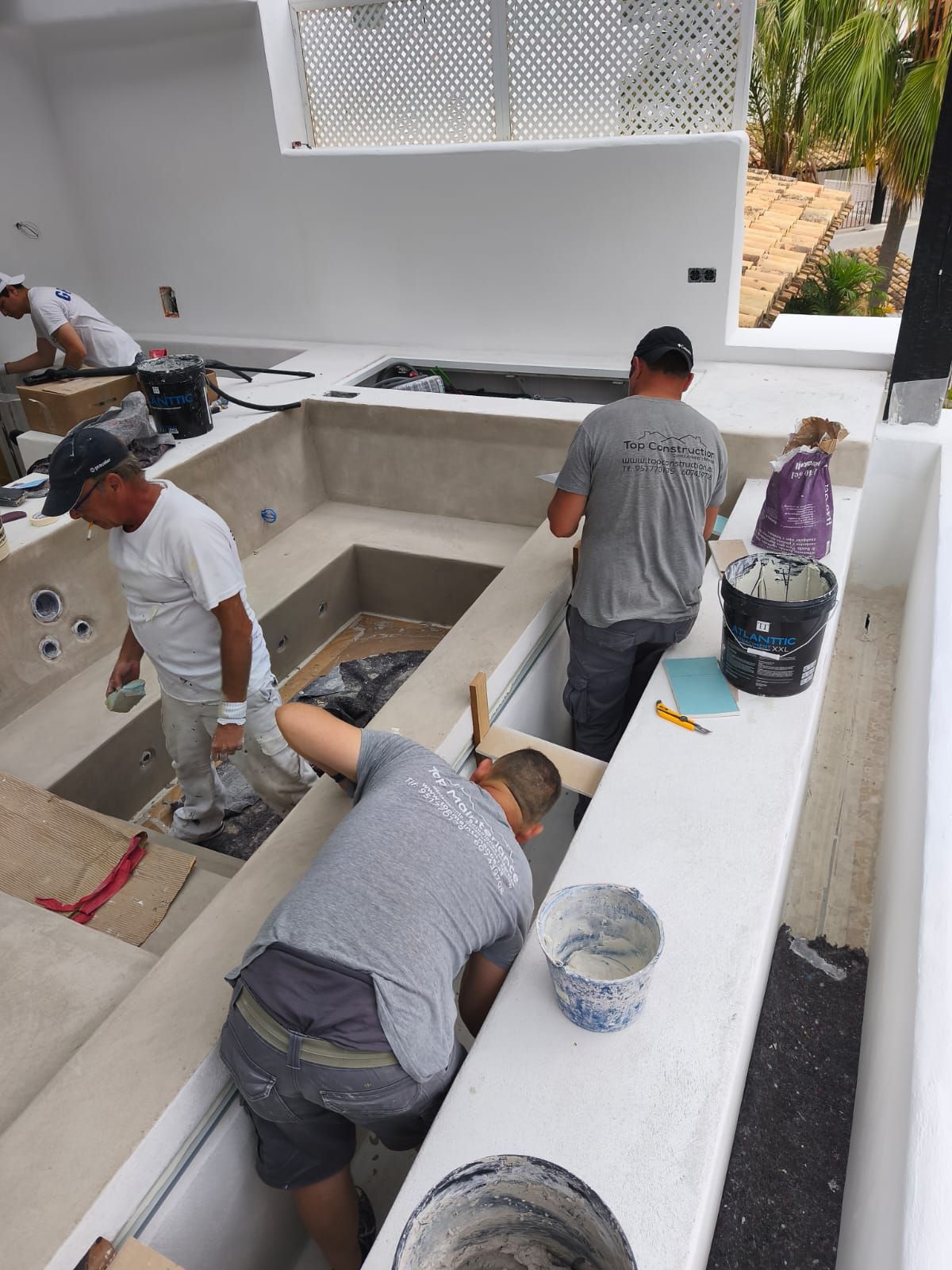 Obreros enyesando una piscina de color claro con escalones y varias secciones. Paredes blancas y brillantes.