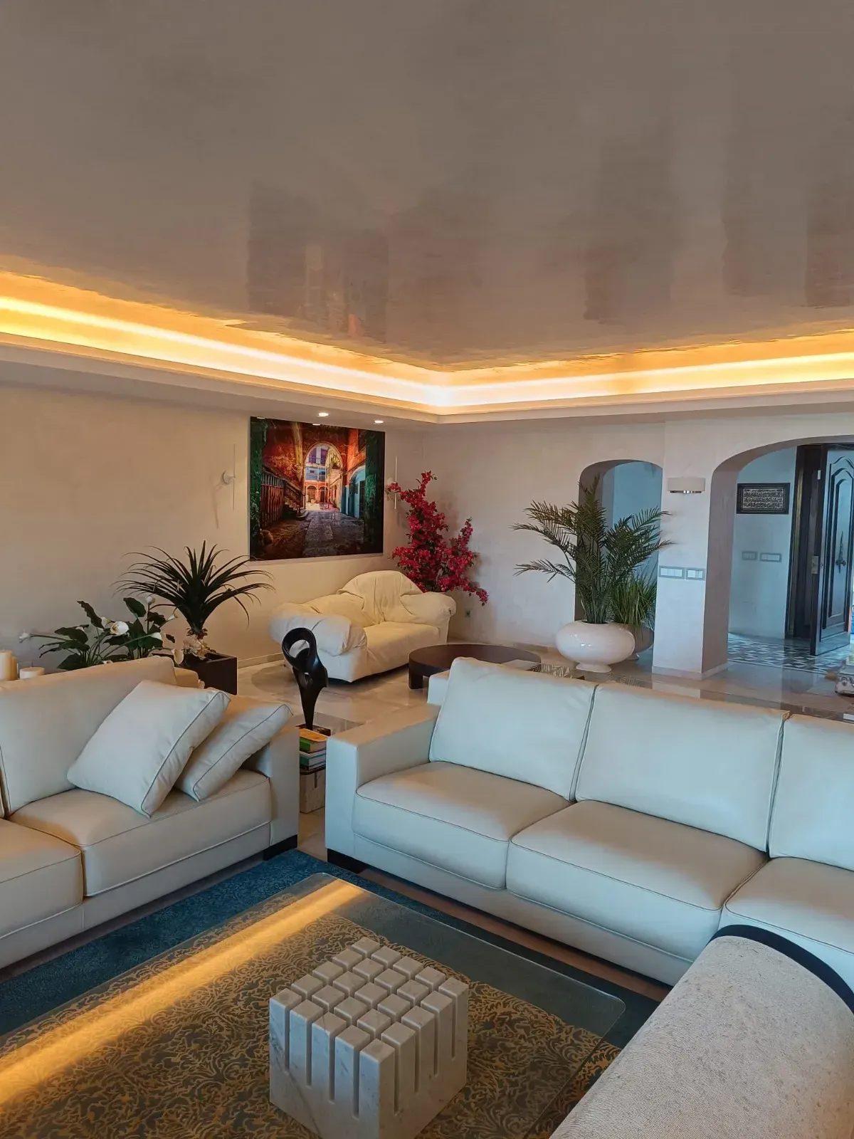 Sala de estar moderna con sofás color crema, arte, plantas e iluminación empotrada.