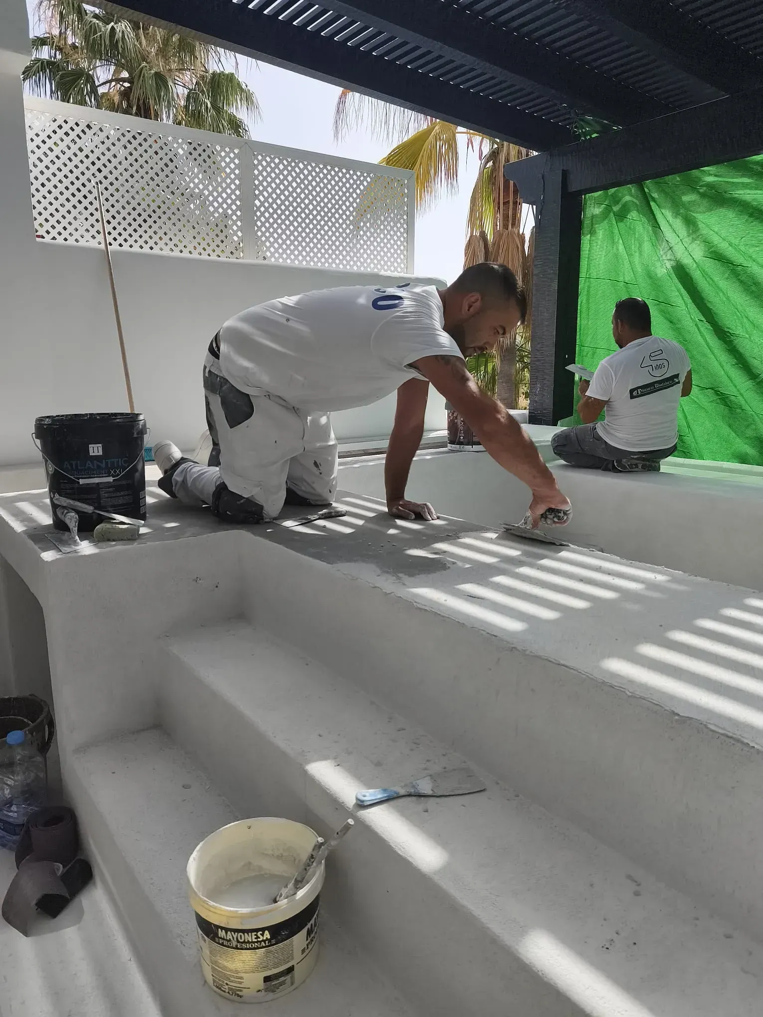 Dos trabajadores pintando una zona de piscina blanca escalonada al aire libre.