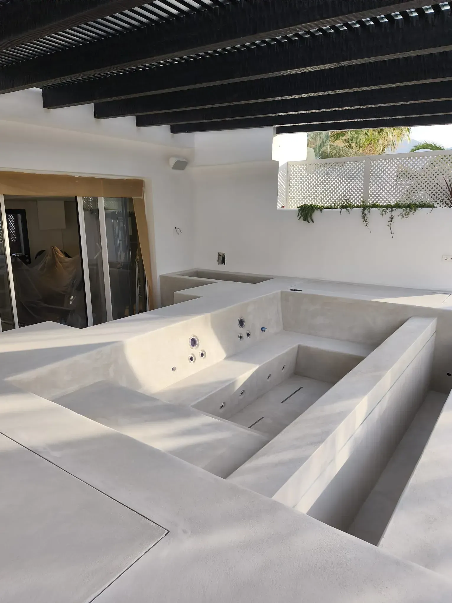 Estructura exterior de hormigón con escalones y asientos hundidos, bajo una pérgola de lamas negras.