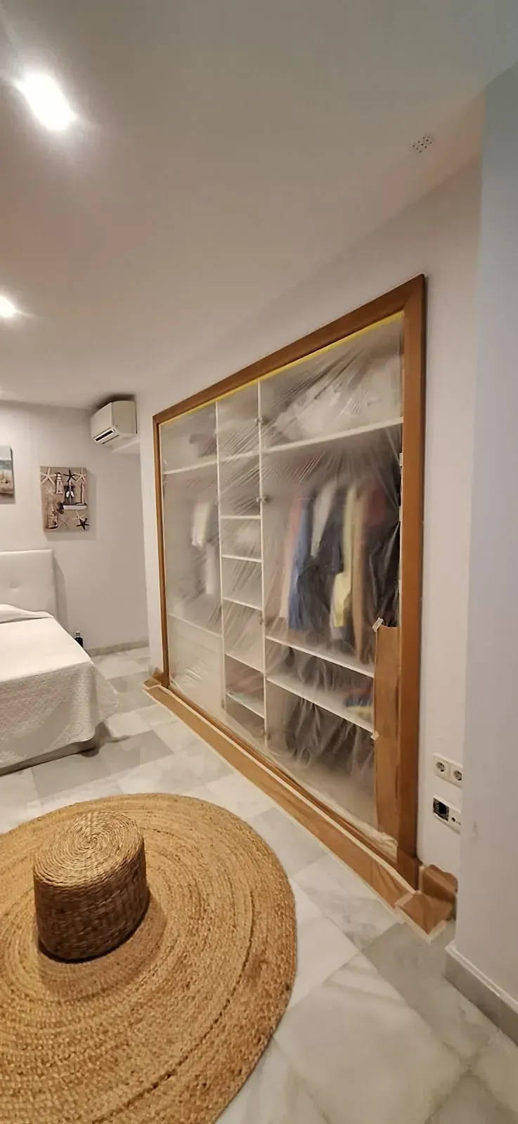 Vestidor con revestimiento de plástico transparente y estructura de madera. Frente a él hay una gran alfombra circular.