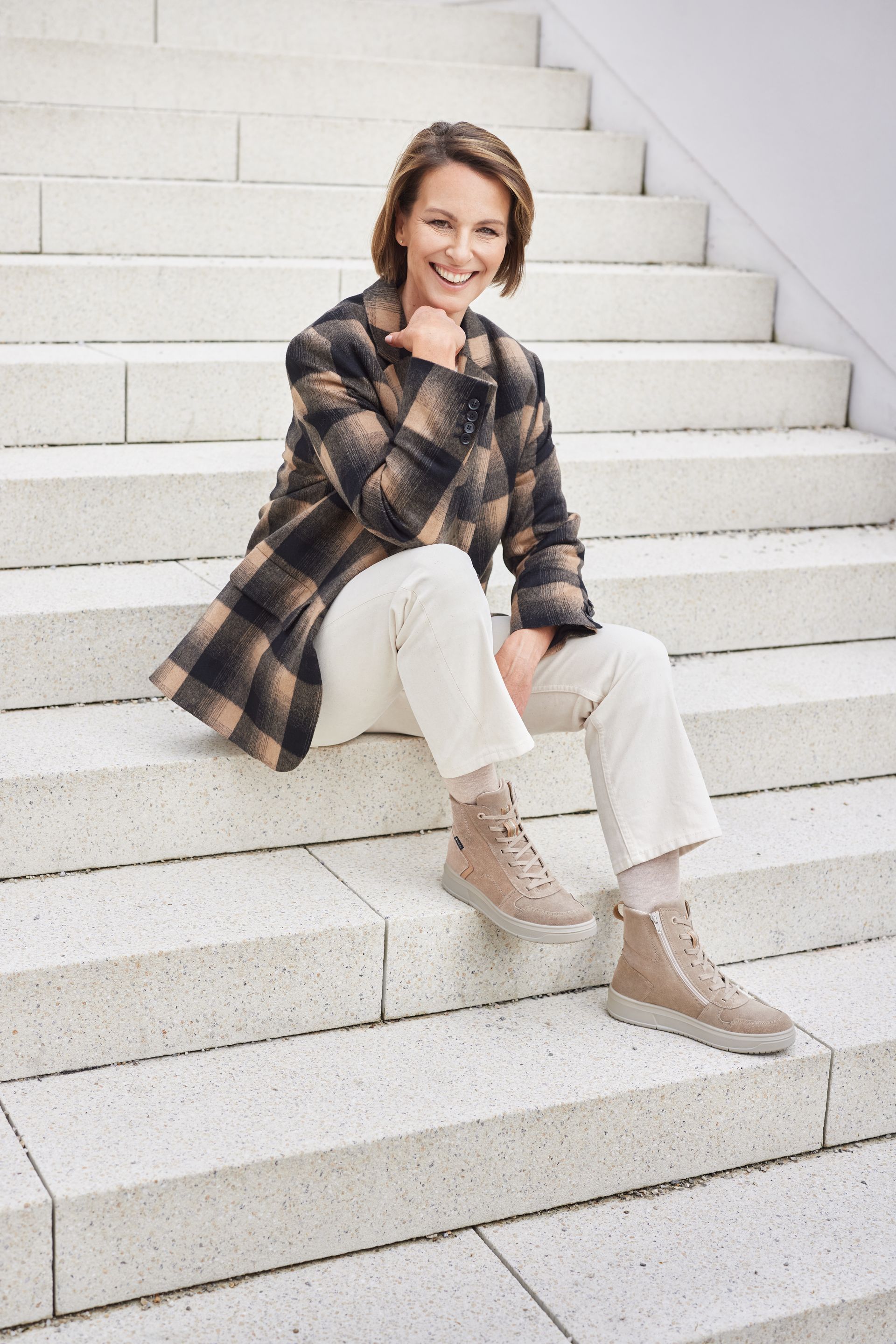 Eine junge Dame mit kariertem Hemd und Sportschuhen sitzend auf einer Treppe