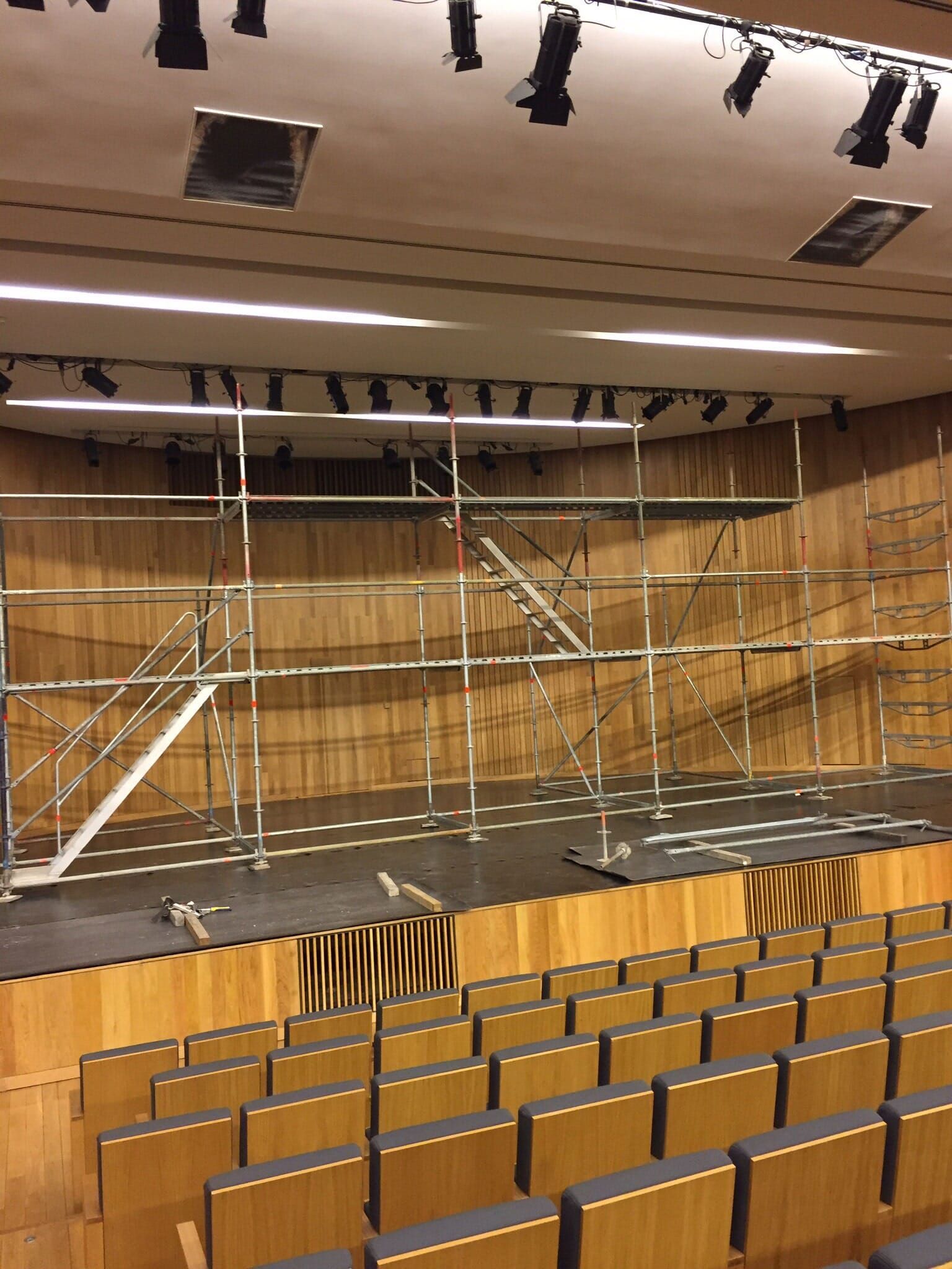 Um grande auditório com assentos de madeira e andaimes no palco.