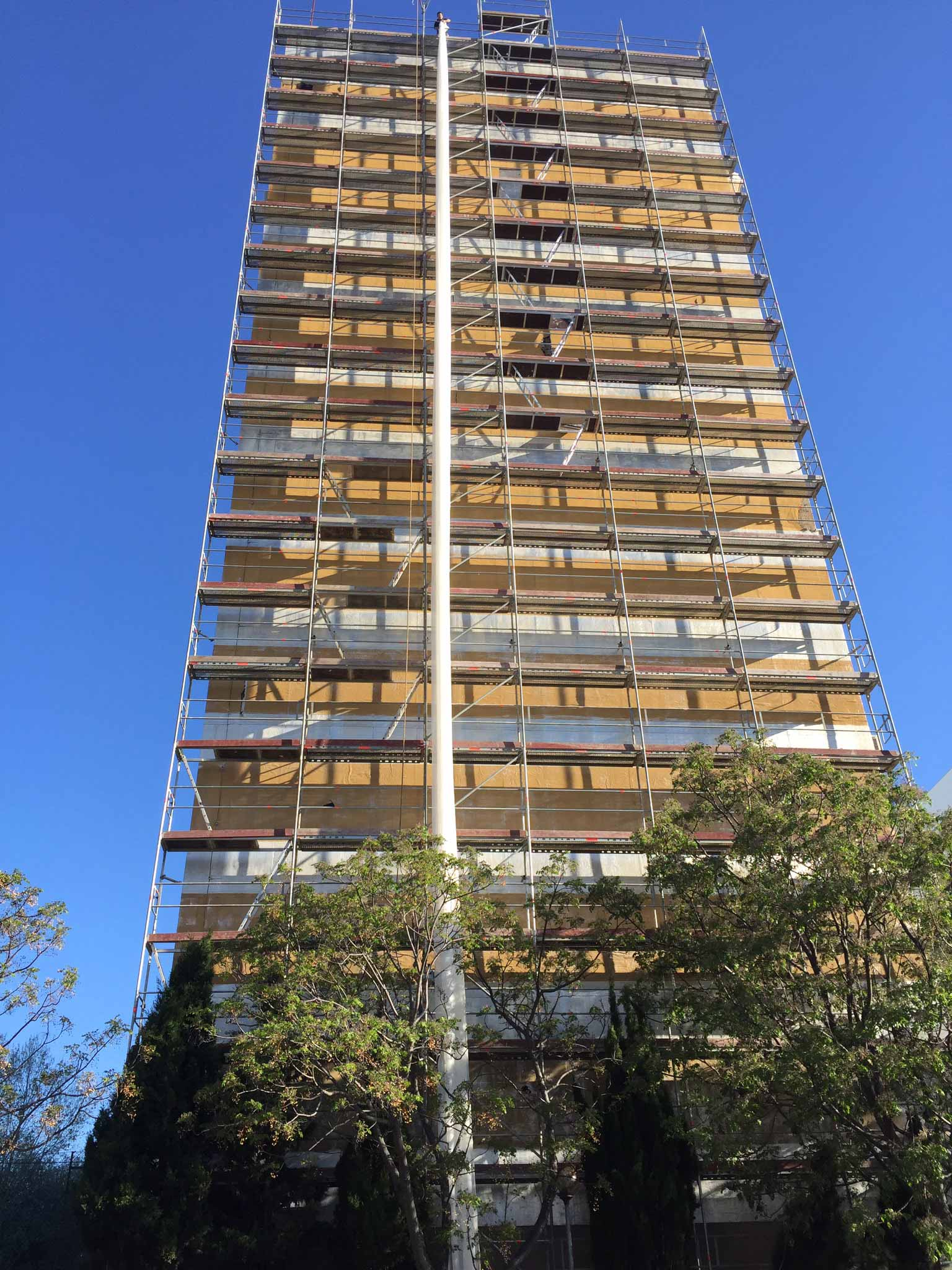 Um edifício alto com andaimes ao redor e árvores na frente dele.