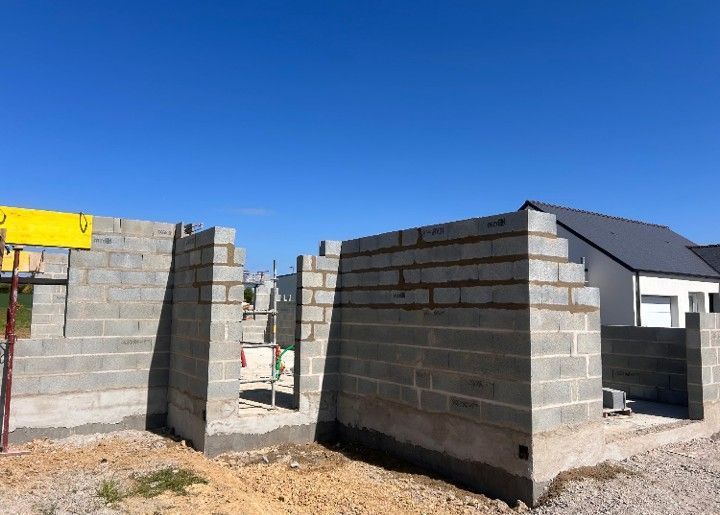 Murs d'une maison en parpaings partiellement construits sous un ciel bleu clair
