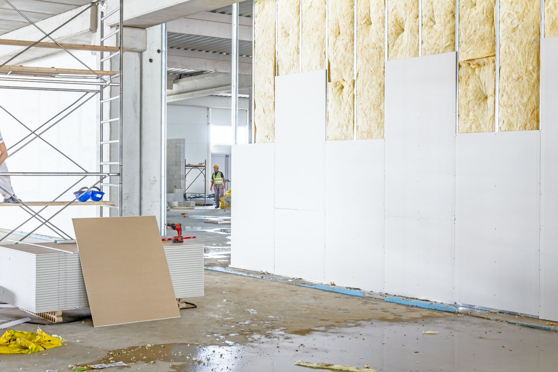Chantier de rénovation intérieure avec échafaudages, isolation apparente et murs blancs inachevés