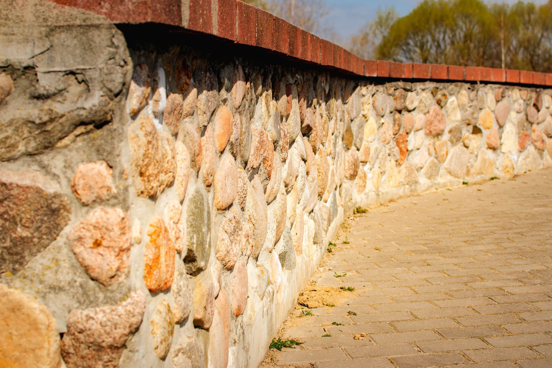 Mur en pierre coiffé d'un chapiteau en briques, bordant une allée pavée en plein jour.
