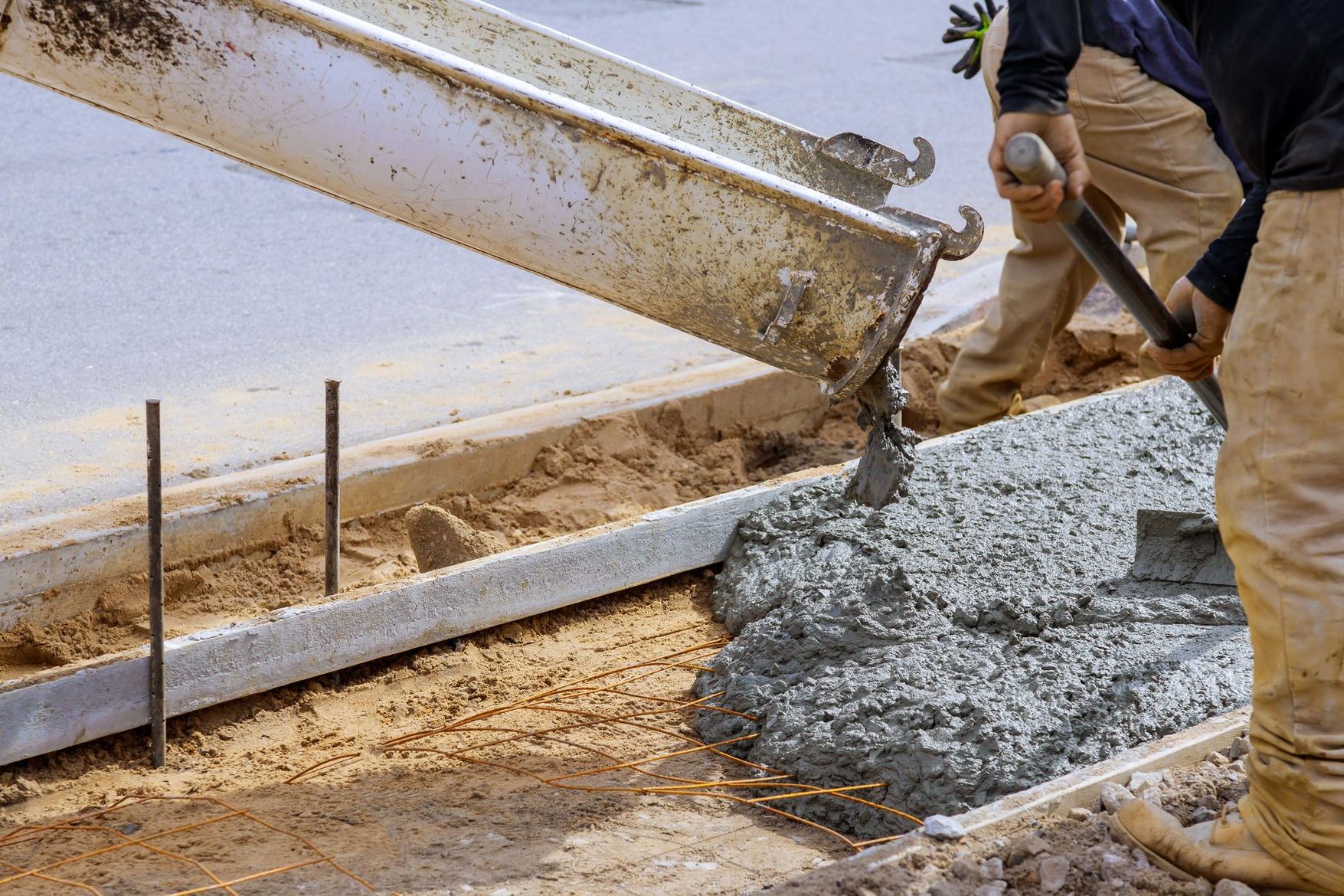 Un ouvrier déverse du béton frais depuis une goulotte sur un chantier de construction et le lisse le long d'un coffrage.