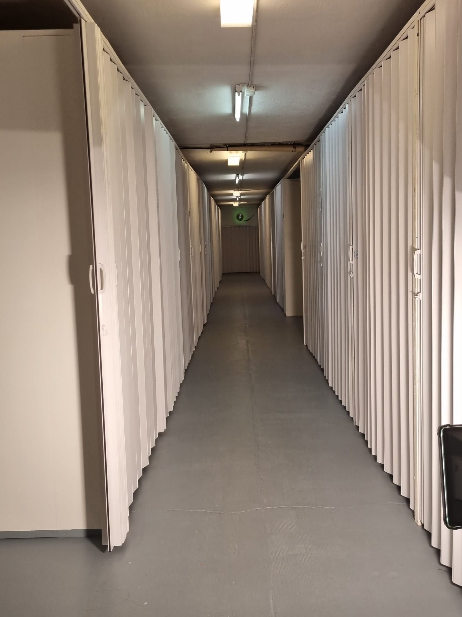 Un long couloir bordé de rangements blancs. Des néons illuminent le sol et le plafond gris.