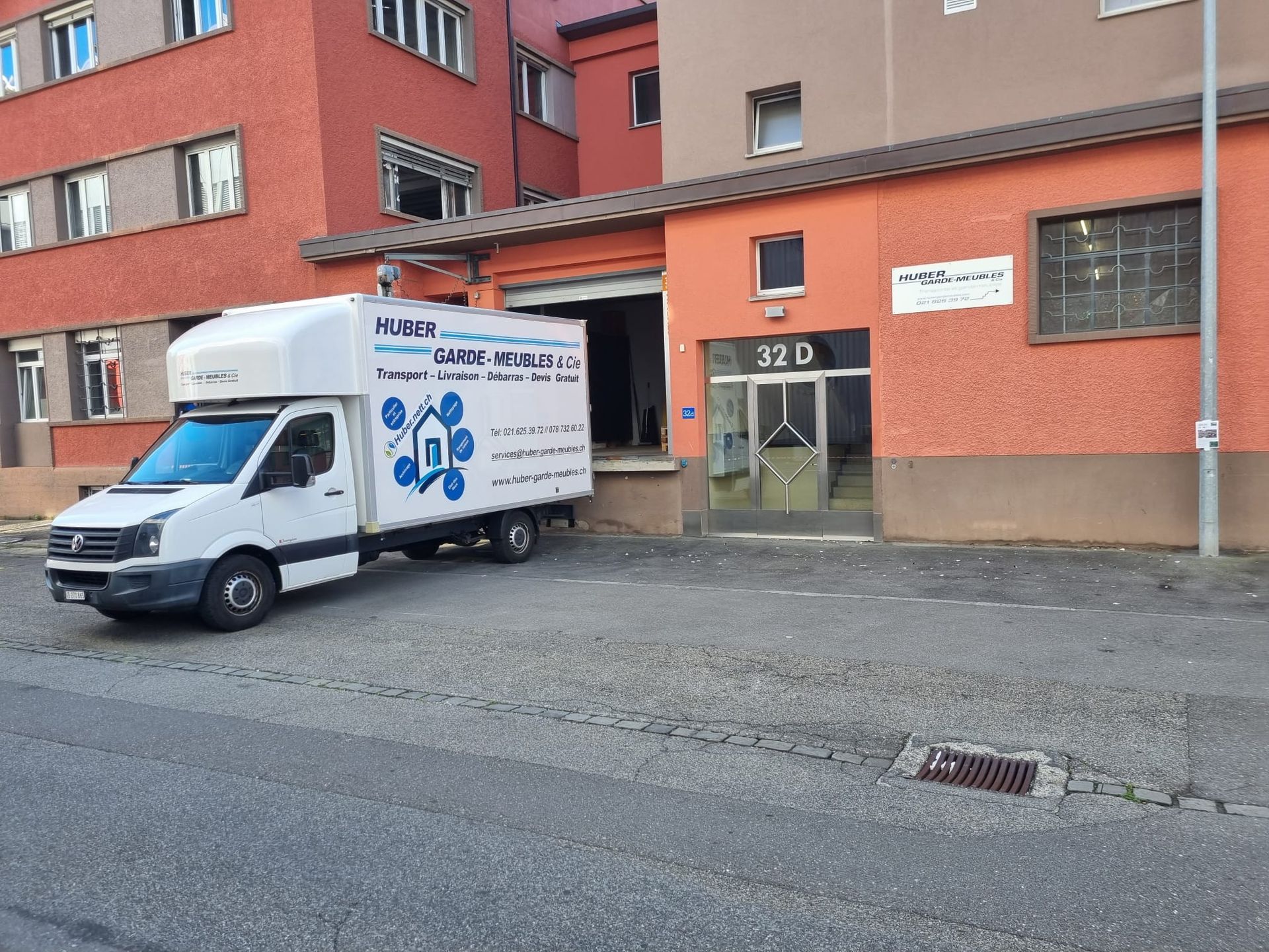 Camion de livraison blanc garé devant un bâtiment en briques.