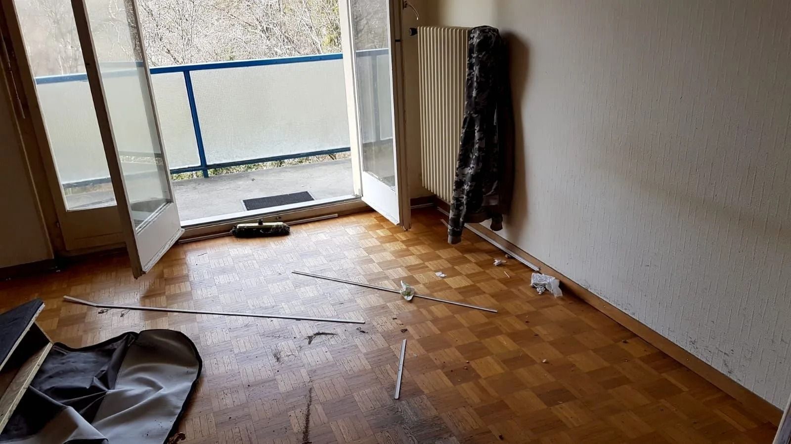 Vue intérieure d'une pièce avec parquet, portes-fenêtres donnant sur un balcon et une bâche noire.