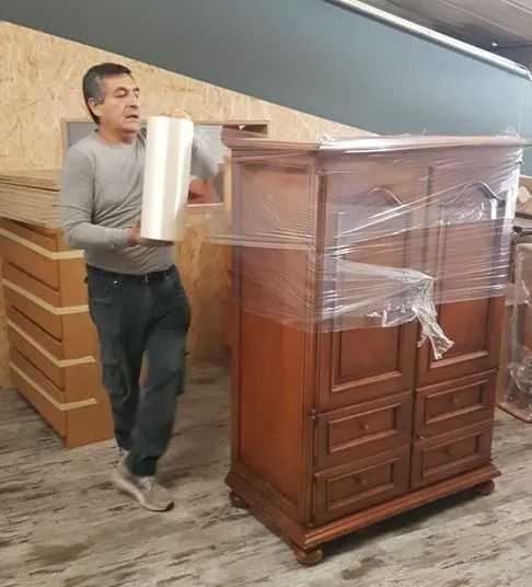 Un homme emballe une armoire en bois avec du film plastique à l'intérieur d'un entrepôt.