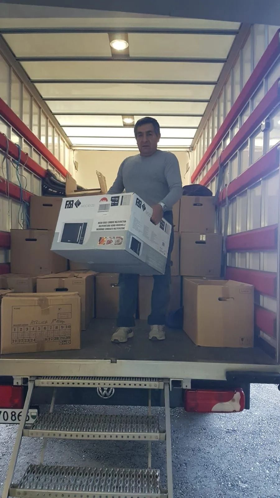 Un homme dans un camion chargeant une grande boîte ; entouré d'autres boîtes.
