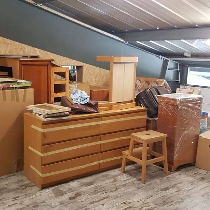 Pièce remplie de meubles et de cartons de déménagement, certains emballés dans du plastique.