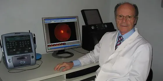 Un hombre con bata de laboratorio está sentado frente a un monitor de computadora.