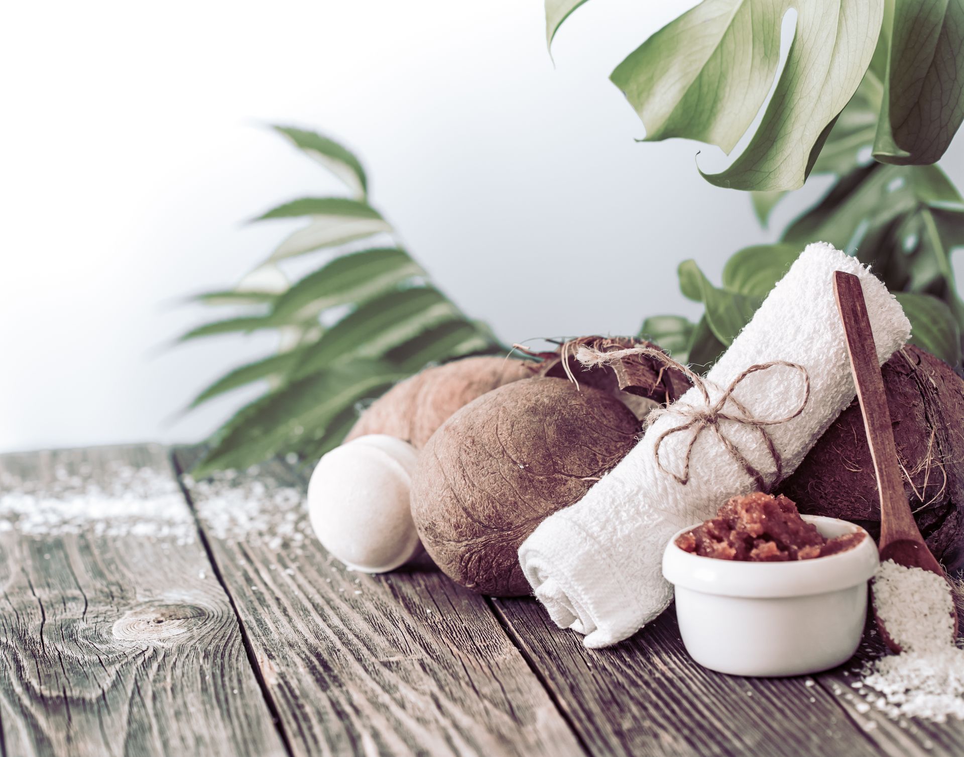 Articles de spa en noix de coco avec serviette blanche et bol sur une table en bois patiné, feuilles vertes en arrière-plan