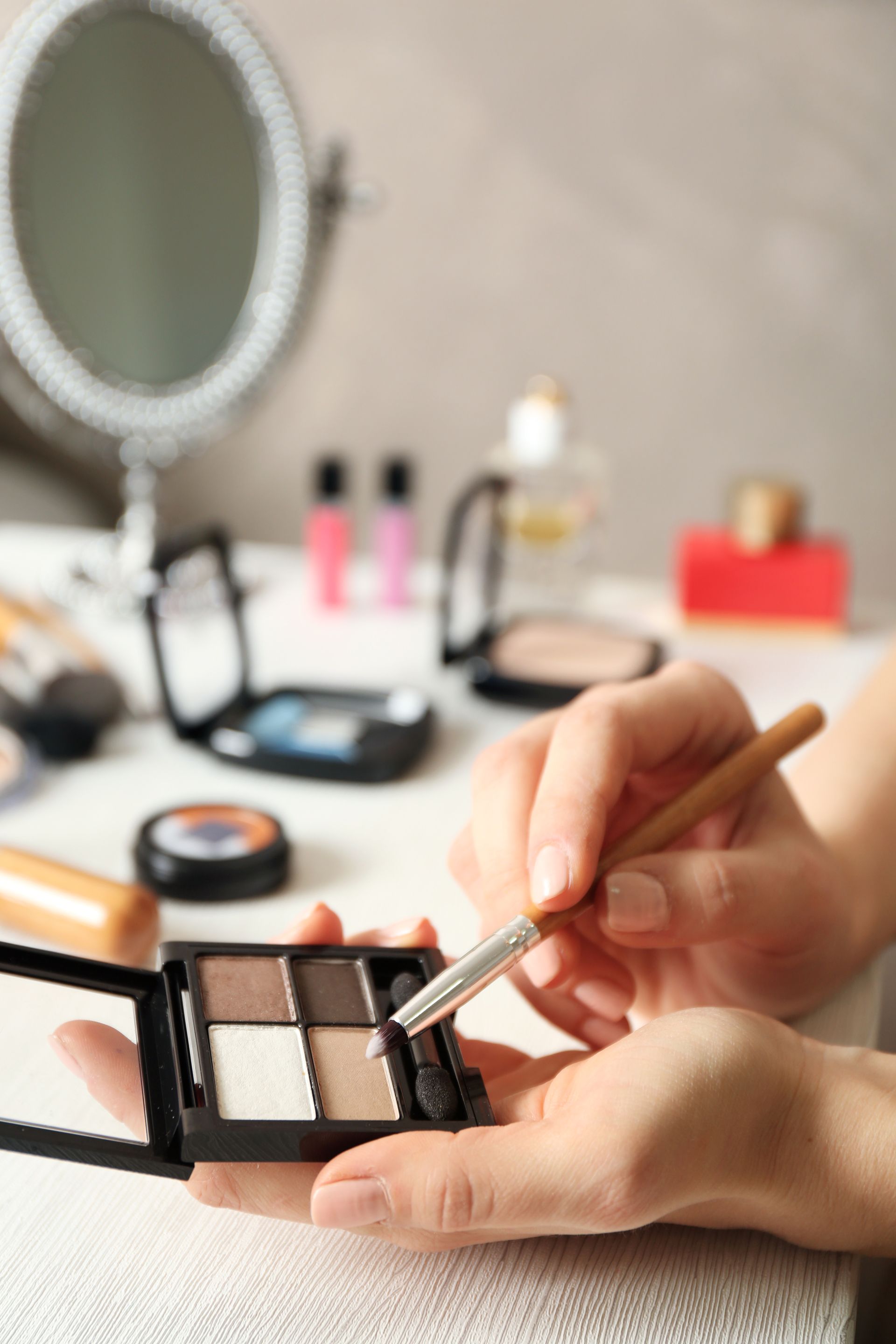 Mains appliquant du fard à paupières avec un pinceau à l'aide d'une palette de maquillage sur une coiffeuse