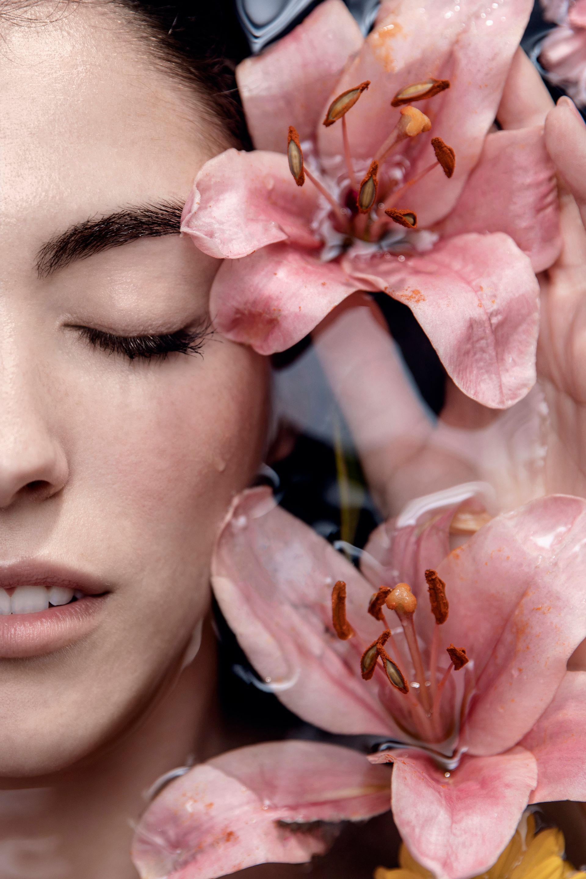 Gros plan sur le visage d'une femme près de fleurs roses, les yeux fermés et sous une douce lumière.