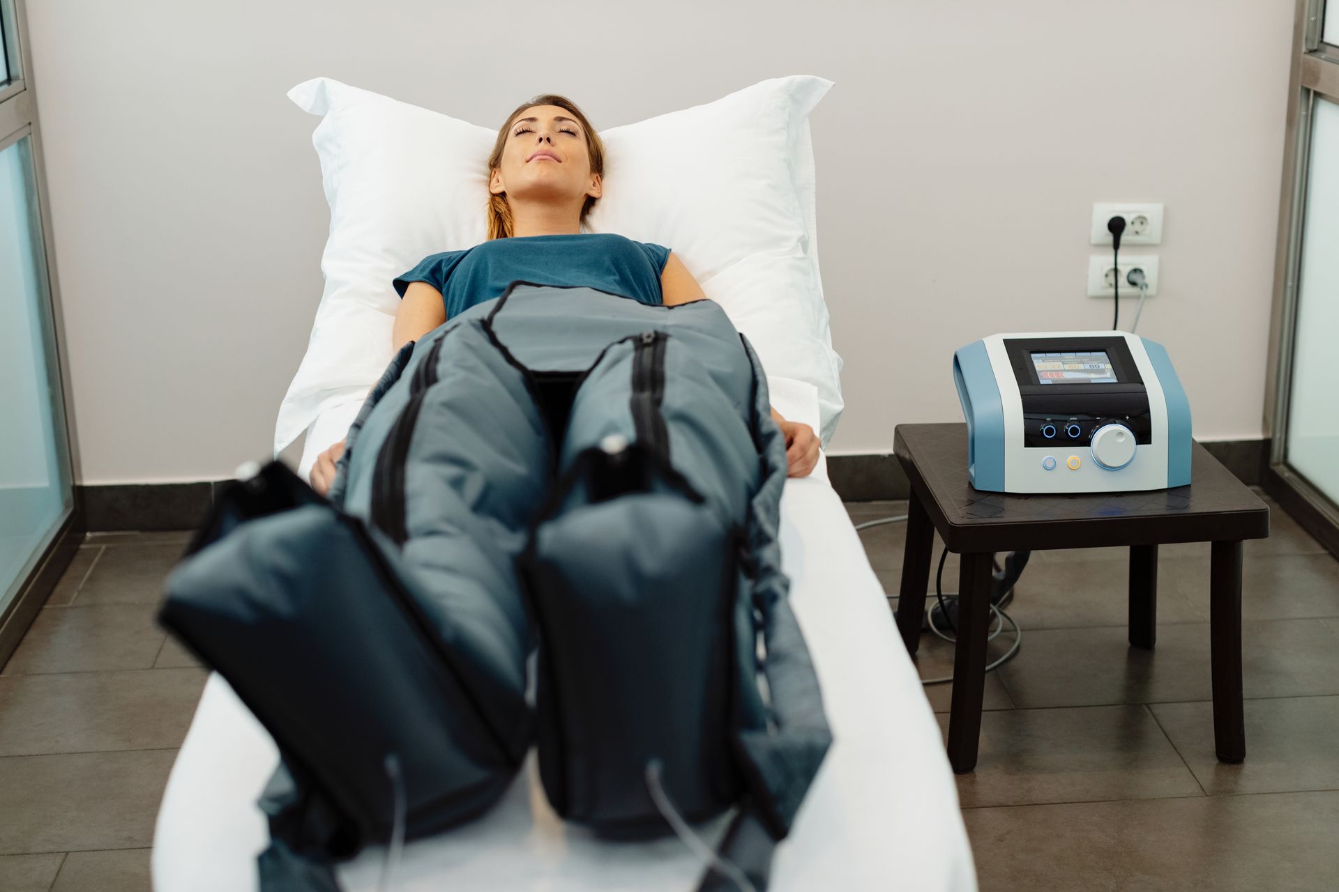 Une personne allongée sur un lit médicalisé avec un appareil de compression des jambes dans une salle de consultation.