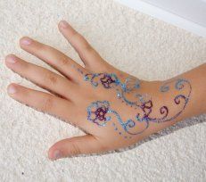 Dos de la main orné d'un motif floral pailleté bleu et violet façon henné
