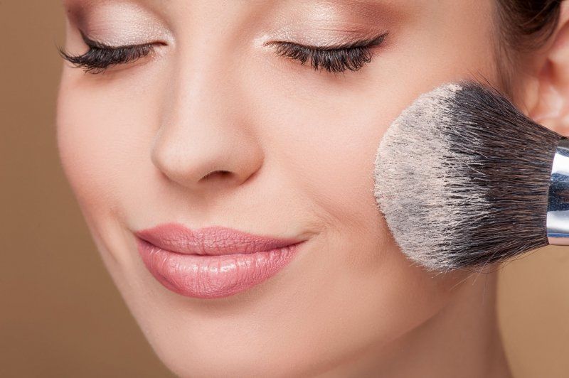 Femme se maquillant la joue au pinceau, les yeux fermés