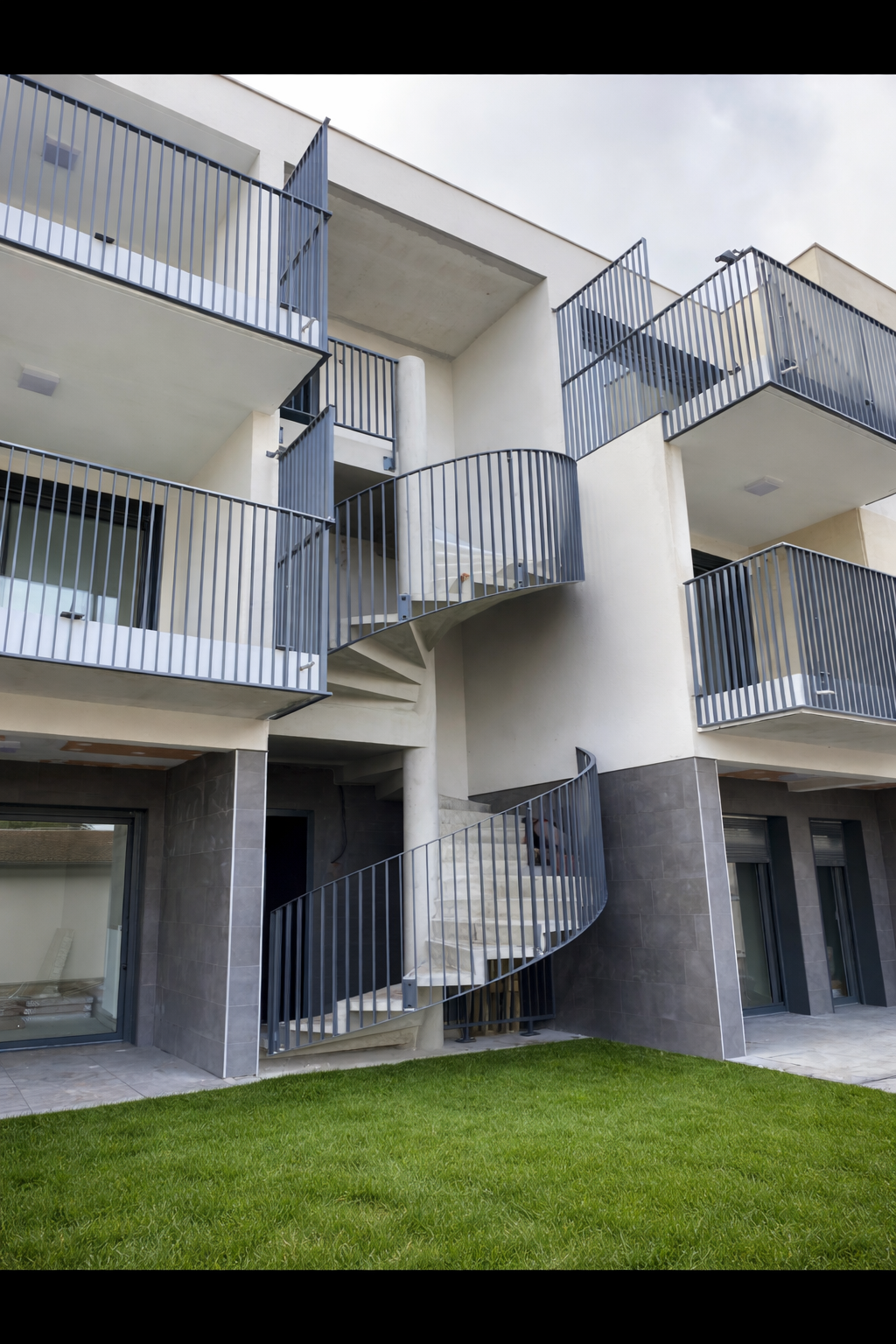 Immeuble d'appartements moderne avec balcons et escaliers en colimaçon donnant sur une pelouse verdoyante
